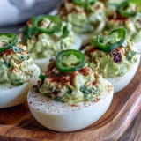 Vibrant deviled eggs filled with zesty guacamole, topped with diced tomato and a sprinkle of smoked paprika.  