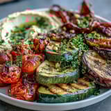 Vibrant summer vegetable platter with hummus, showcasing charred zucchini, bell peppers, and cherry tomatoes served with tahini dip.  