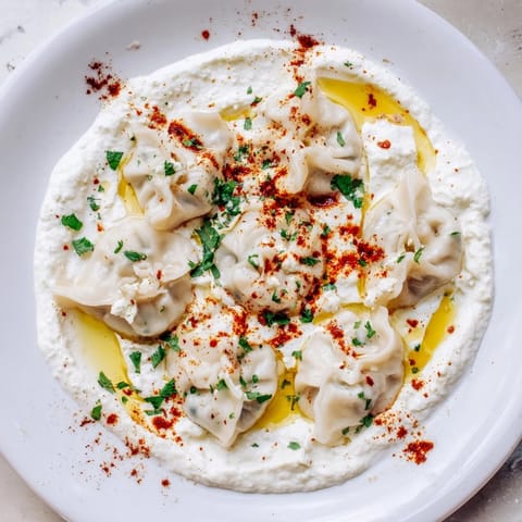 A close-up of steaming Turkish cheesy manti, soft dough and vibrant red spiced butter sauce.