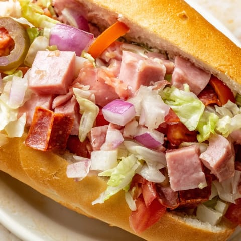Hearty chopped Italian grinder sandwich in a golden hoagie roll, loaded with meats, cheese, and tangy dressing.