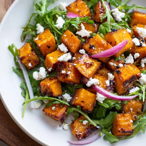 A vibrant bowl of Roasted Sweet Potato Salad features golden cubes, red onion slices, and crunchy pumpkin seeds.  