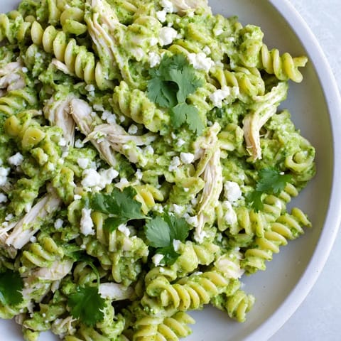 Cilantro Lime Chicken Pasta served in a white bowl with crumbled feta cheese and fresh lime wedges.