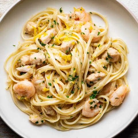 A serving of Lemon Garlic Shrimp & Chicken Pasta plated with lemon wedges and parsley, showcasing tender shrimp and chicken pieces tossed through strands of al dente pasta.