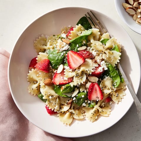 Spring spinach strawberry pasta salad in a white bowl features al dente farfalle, vibrant greens, and sweet berry slices, perfect for a light lunch or picnic.  