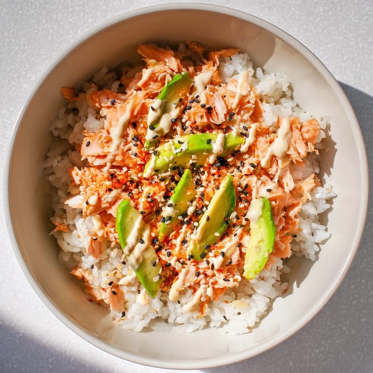 The Emily Mariko Salmon Rice Bowl features tender salmon, fluffy rice, and vibrant avocado slices drizzled with spicy mayo for a quick meal.