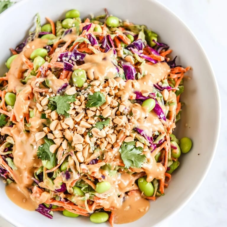Crunchy Thai Peanut Salad served in a white bowl, garnished with fresh cilantro, sesame seeds, and lime wedges, perfect for a light vegan lunch.  