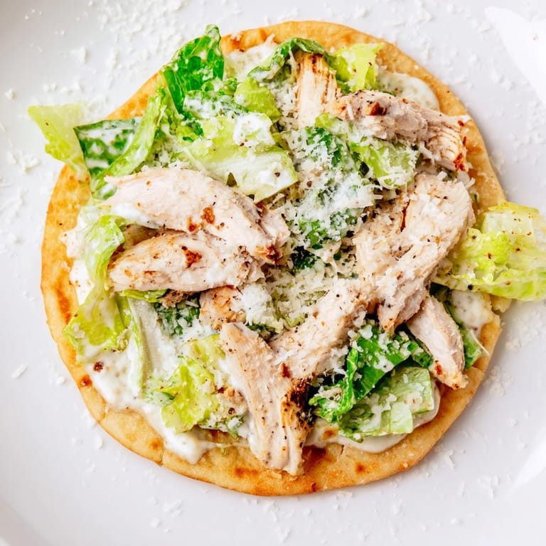 This Chicken Caesar Flatbread features a baked naan crust loaded with fresh romaine and tender sliced chicken.  