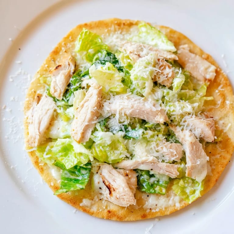 Sliced grilled chicken rests on a warm Chicken Caesar Flatbread, garnished with parmesan and fresh cherry tomatoes.